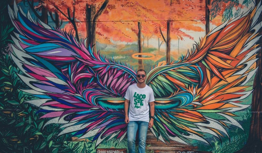 a boy posing behind a mural artwork of an angel's wing